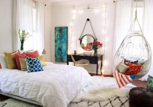 White hanging chair in bedroom with bright pillows